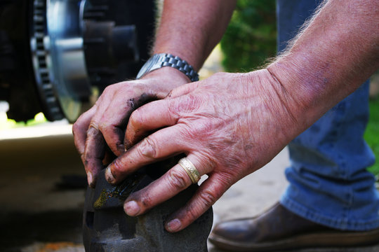 Wrinkled, greasy hands of a man working with automotive parts