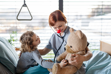 Friendly female doctor examining small girl in bed in hospital.