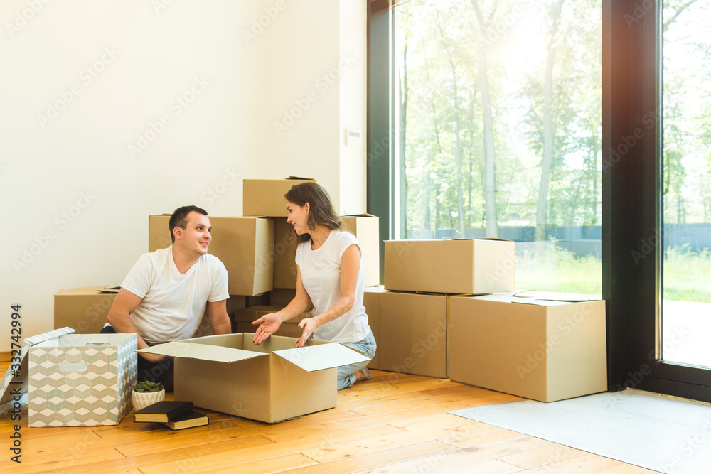 Wall mural Happy young family, parents daughter and son, unpacking boxes and moving into a new home. funny kids run in with boxes