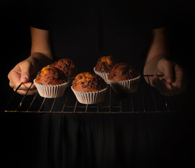 woman with tray of vegan chocolate muffins, black background dark food
