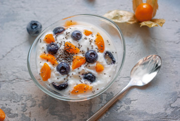 Breakfast yogurt in a glass bowl with blueberries and physalis on a concrete background