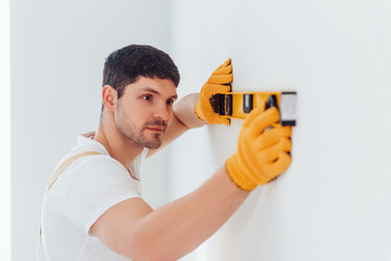 Handyman in yellow uniform checks levels of wall. House renovation conception