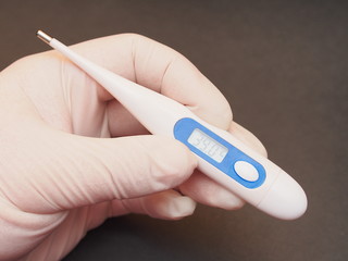 The electronic thermometer is held by a hand in a medical rubber glove. The display shows 39...