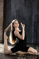 Fototapeta premium A young girl in black sportswear does yoga and shows a sign ok because yoga is not complicated