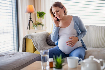 Portrait of pregnant woman in pain indoors at home, making emergency call.