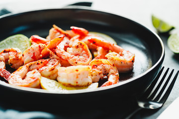 Fried tiger shrimp with lime, lemon and spices on a black plate. Healthy dinner or lunch concept.