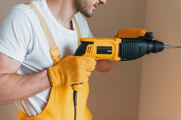 Handyman in yellow uniform works indoors by using hammer drill. House renovation conception