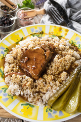 Stewed pork neck in gravy served with barley on wooden table.