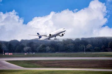Big jet is taking off in blue cloudy sky over the forest.