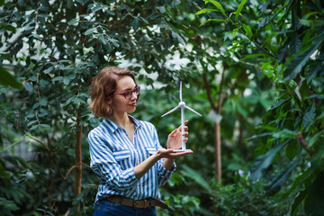 Young woman standing in botanical garden, holding windmill model.