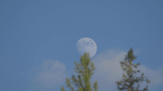 Close up in the daytime blue sky with clouds and a rising moon