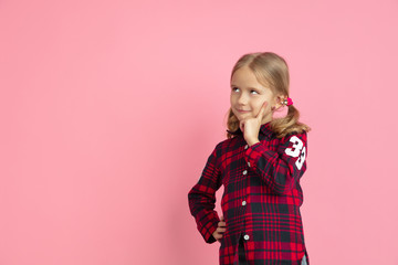 Thoughtful, dreaming. Caucasian little girl's portrait on pink studio background. Beautiful female model with blonde hair. Concept of human emotions, facial expression, sales, ad, youth, childhood.