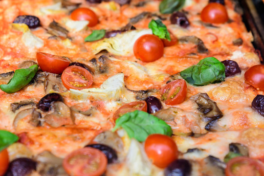 Traditional Italian pizza with fresh tomatoes, artichoke, mushrooms and olives displayed for sale at a street food market festival in Bucharest, Romania, healthy food photographed with soft focus