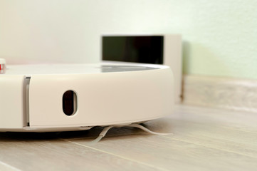 Robotic vacuum cleaner on laminate wood floor charging from base station.