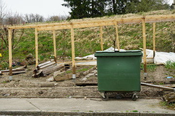 wooden skeleton or frame of a greenhouse in a allotment garden with a bin for organic waste in the foreground