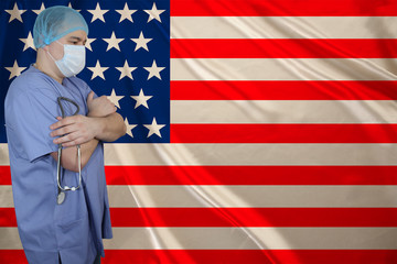 male doctor in a medical mask with a stethoscope in his hand against the background of the USA silk national flag, concept of national medical care, health, insurance, tourism