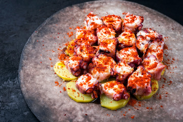 Traditional Spanish pulpo a la gallega with barbecued octopus, potato chips and chili as closeup on a modern design plate with copy space left