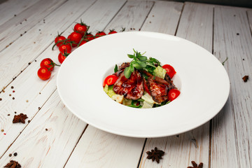 Vegetable salad with meat and barbecue sauce served on a large round white plate. Restaurant dish on a wooden background.