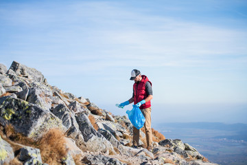 Obraz premium Man hiker picking up litter in nature in mountains, plogging concept.