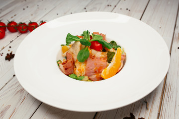 Salad of various vegetables and fresh salmon. Restaurant dish on a wooden background. The table is decorated with tomatoes and star anise.