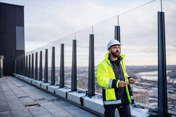 Man engineer walking on construction site, holding tablet.