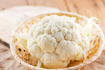 Cauliflower in a wicker basket on wooden background. Organic cauliflower on the burlap. Vegan food. Rustic style