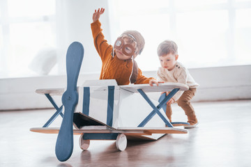 Two little boys in retro pilot uniform having fun with toy plane indoors © standret