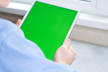 Man touches and looks at the screen of the tablet with a green screen. Chroma key on the screen of the tablet