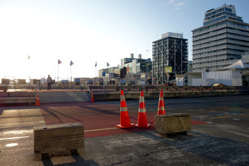 looking at a cutout of the cityline of Auckland near the seaside. Buildings some of them under construction and other urban elements are shown. The morning sun creates a beautiful scenery.