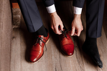 groom tied the laces on the shoes close up. business man is hanging shoes indoor in hotel room....