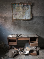 Escritorio con mapa en la pared en habitación sucia de casa abandonada.