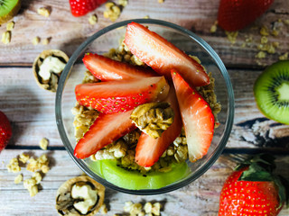 Healthy nutrition. Delicious granola breakfast with yogurt, kiwi, strawberries and nuts on a wooden background.