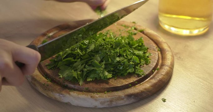 Cutting up parsley on chopping board, healthy food. Parsley cutting in kitchen. Woman using knife to cut. Closeup of knife and female hand