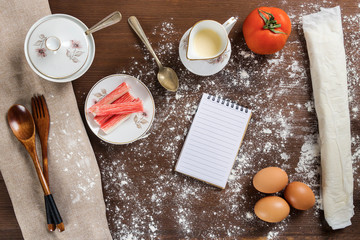 Set of ingredients and raw dough on a floured wooden table. Small notebook with space to write the shopping list or ingredients to cook a healthy recipe. © Graphic PhotoArt