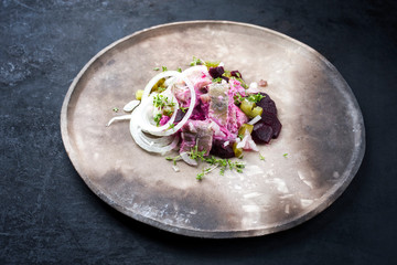 Traditioneller Matjes Hering mit rote Beete Salat und ZwiebelrInge angeboten als closeup auf einem rustikalen Modern Design Teller mit Textfreiraum