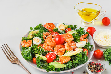 Caesar salad with shrimps, avocado, parmesan cheese, tomatoes and kale with fork on white background. Healthy food