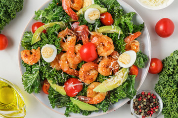 Shrimp caesar salad with avocado, parmesan cheese, tomatoes, eggs and kale on white marble table. top view