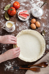 Vertical top view of a person preparing the raw dough to be filled with the necessary ingredients to cook a healthy recipe such as a salty tart or a quiche. Cooking at home.
