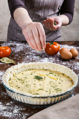 Woman scattering chopped parsley over ingredients inside raw dough to cook a healthy recipe like salty tart or quiche. Cooking at home.