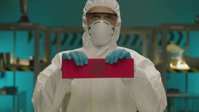 Portrait of masked laborant . Concept of coronavirus quarantine. MERS-Cov. Novel coronavirus. Doctor with a overall safety uniform Tear the red paper with the word coronavirus. COVID-2019 or nCoV2019