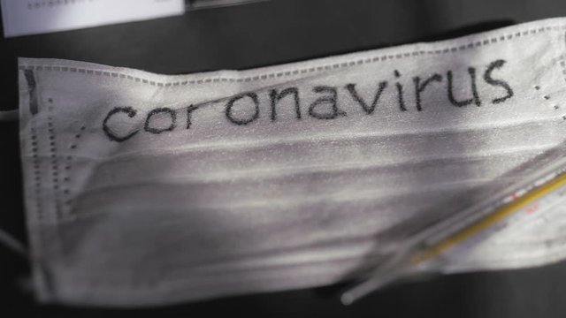 Coronavirus. Medical disposable gauze bandages are on the table. A mercury glass thermometer rests on a protective medical mask.