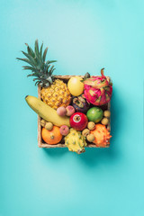 Tropical fruits on blue background. Rattan box full of exotic thailand fruits - pineapple, pitahaya, kiwano, african horned melon, tamarillo fruit, granadilla, feijoa, salak, snake fruits, maracuya