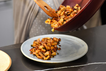 Hash mix being served from frying pan onto blue ceramic plate