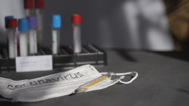 Coronavirus. Medical test tubes are in the organizer. Medical disposable gauze bandages are on the table. A mercury glass thermometer rests on a protective medical mask.