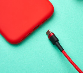 red smartphone and cable in textile braid on a green background