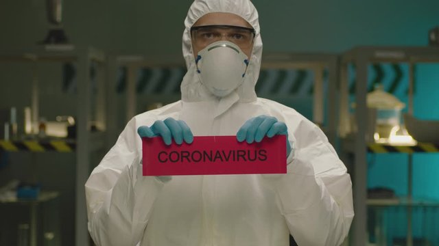 Portrait of masked laborant . Concept of coronavirus quarantine. MERS-Cov. Novel coronavirus. Doctor with a overall safety uniform Tear the red paper with the word coronavirus. COVID-2019 or nCoV2019