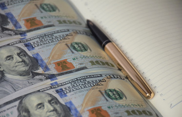 money book, gold pen on a diary with straight rows of banknotes, US dollars on a white background