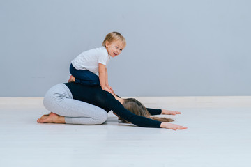 Fototapeta premium Beautiful mother and charming little daughter are smiling while practicing yoga together at home, making child's pose exercise, copy space