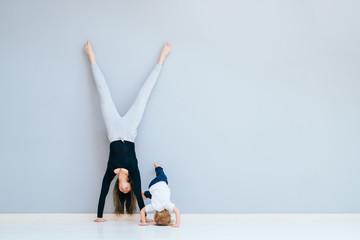 Sportive brunette mother with baby son doing press exercise on grey yoga mat over gray wall background. Athletic and healthy motherhood. Fitness, happy maternity and healthy lifestyle concept.