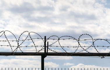 Coiled barbed wire fence and blue sky with clouds